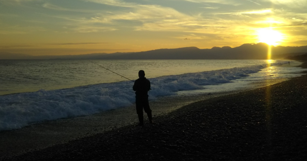 海岸で夕日を浴びている釣り人